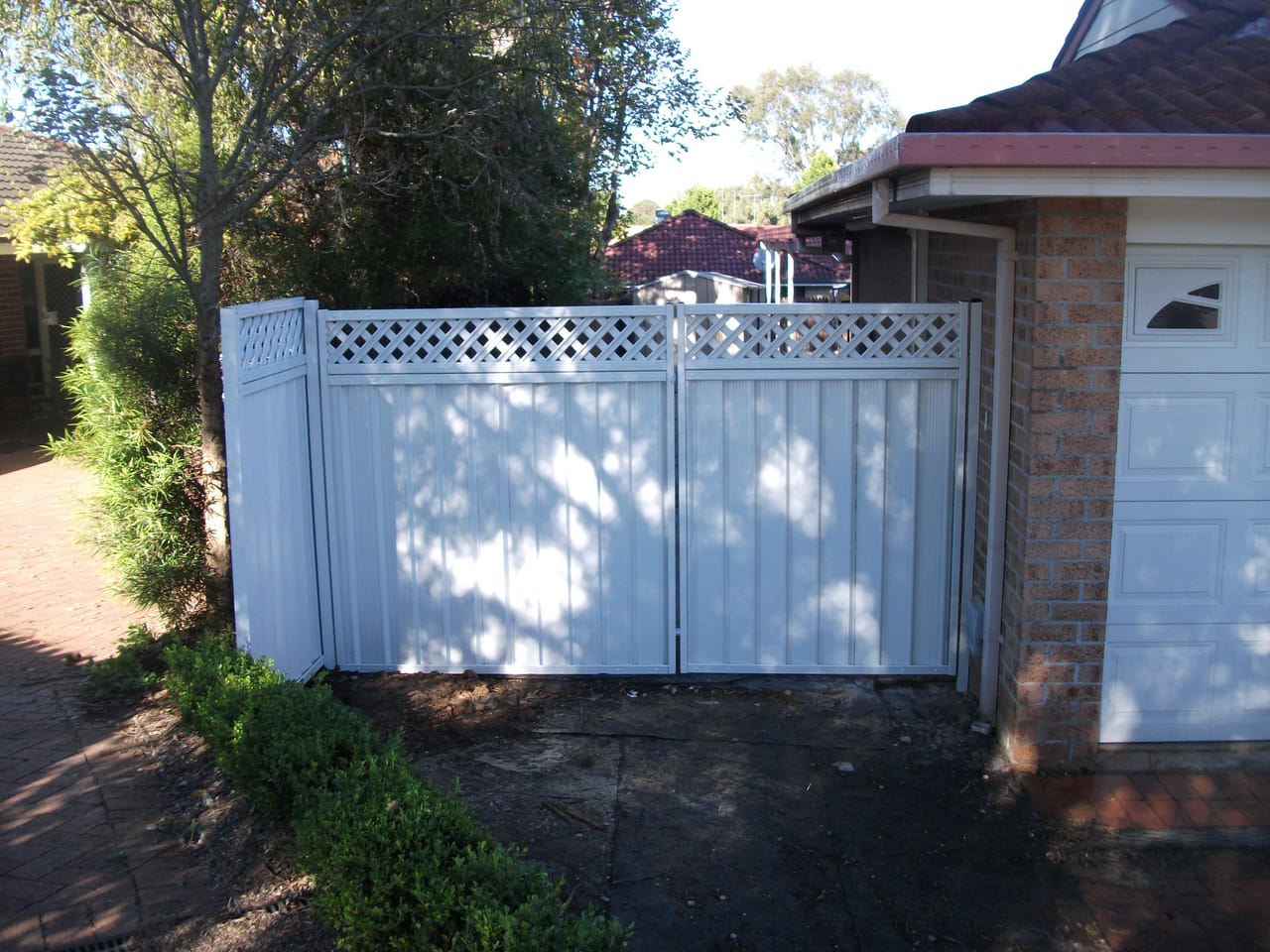 Painted timber double driveway gates with lattice top panels installed across a residential driveway in Sydney